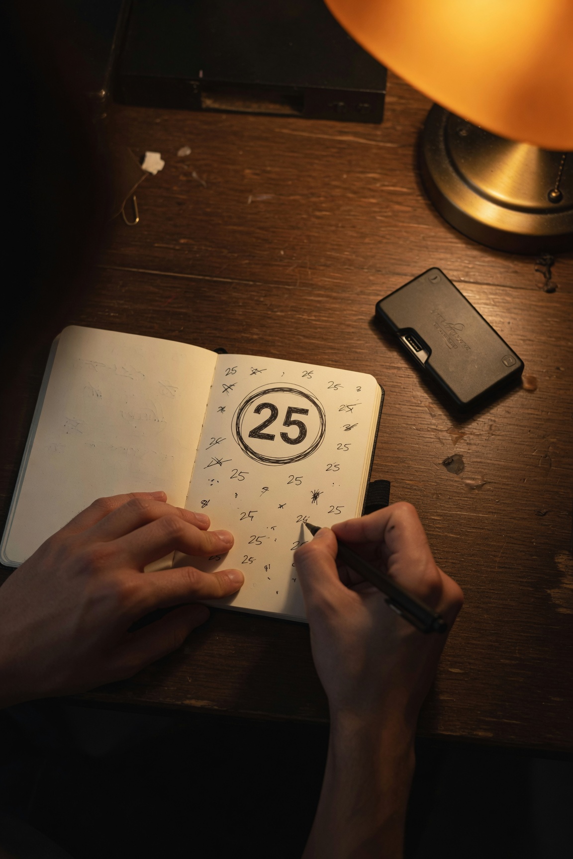 Hands writing a passphrase note beside a hardware wallet, the number 25 circled